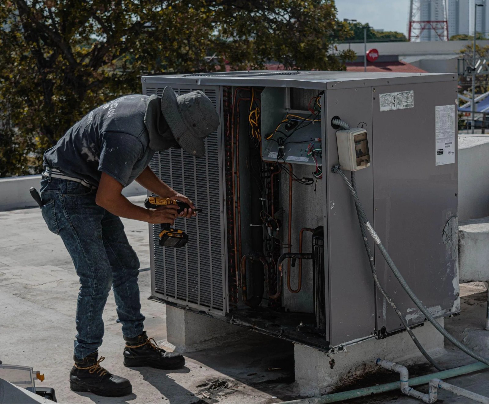 Picture of an HVAC technician servicing an outdoor condenser unit with a cordless drill